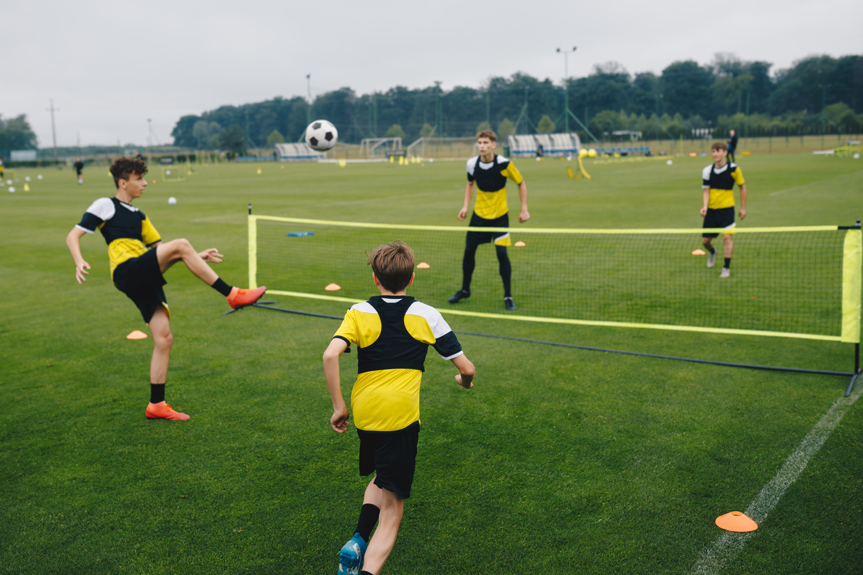 Young boys in youth soccer club playing football tennis training game. Teenage soccer players playing football tennis on training session. Teenagers practicing soccer on grass pitch.